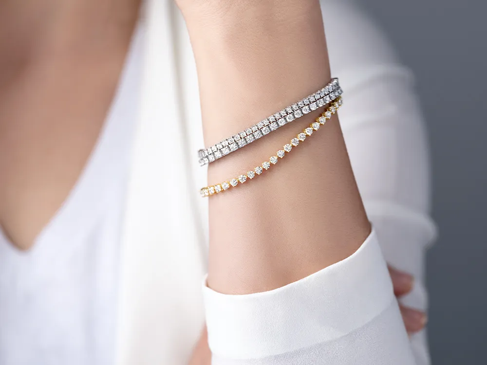 Two diamond tennis bracelets, one silver and one gold, on a wrist.