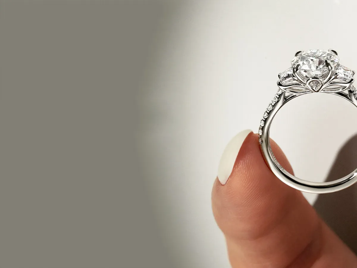 A hand holding a diamond engagement ring with intricate detailing on the band.