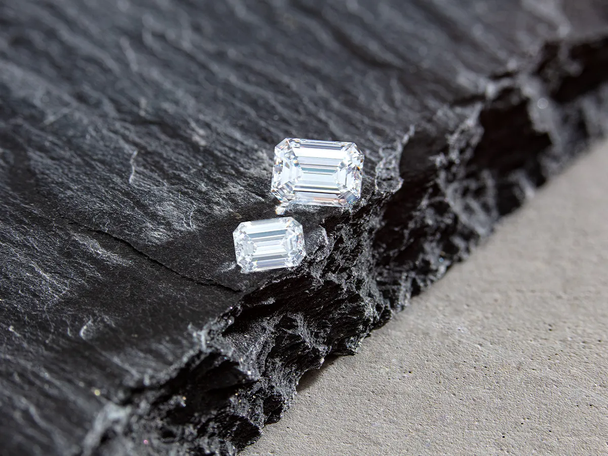 Two emerald-cut diamonds on textured black slate surface.