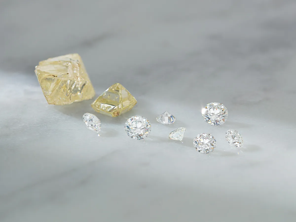 Various cut and uncut diamonds displayed on a marble surface.