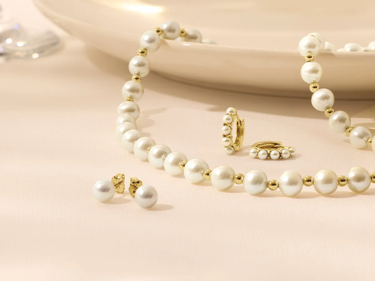 Pearl and gold jewelry set displayed on a soft beige background.