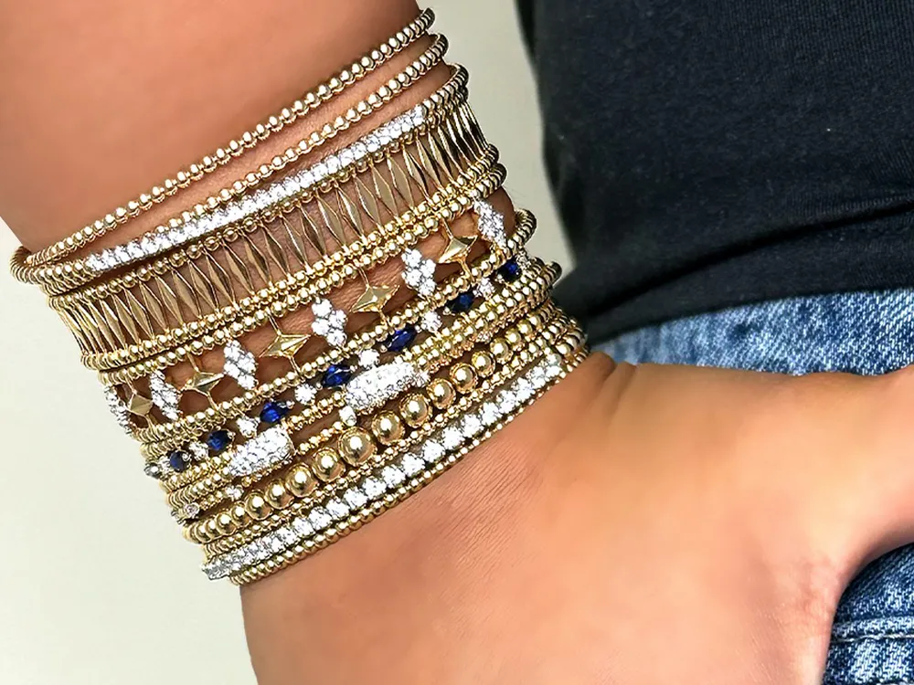 A wrist adorned with multiple gold and diamond bracelets in intricate designs.