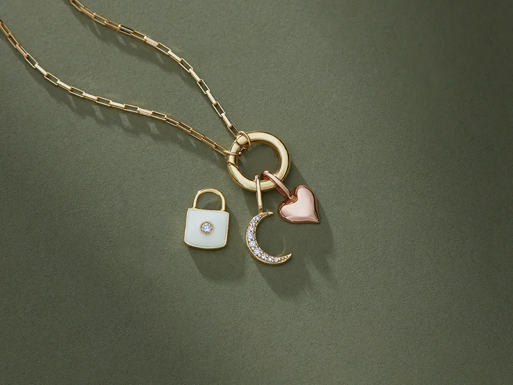 Gold necklace with lock, crescent moon, and heart charms on a green background.