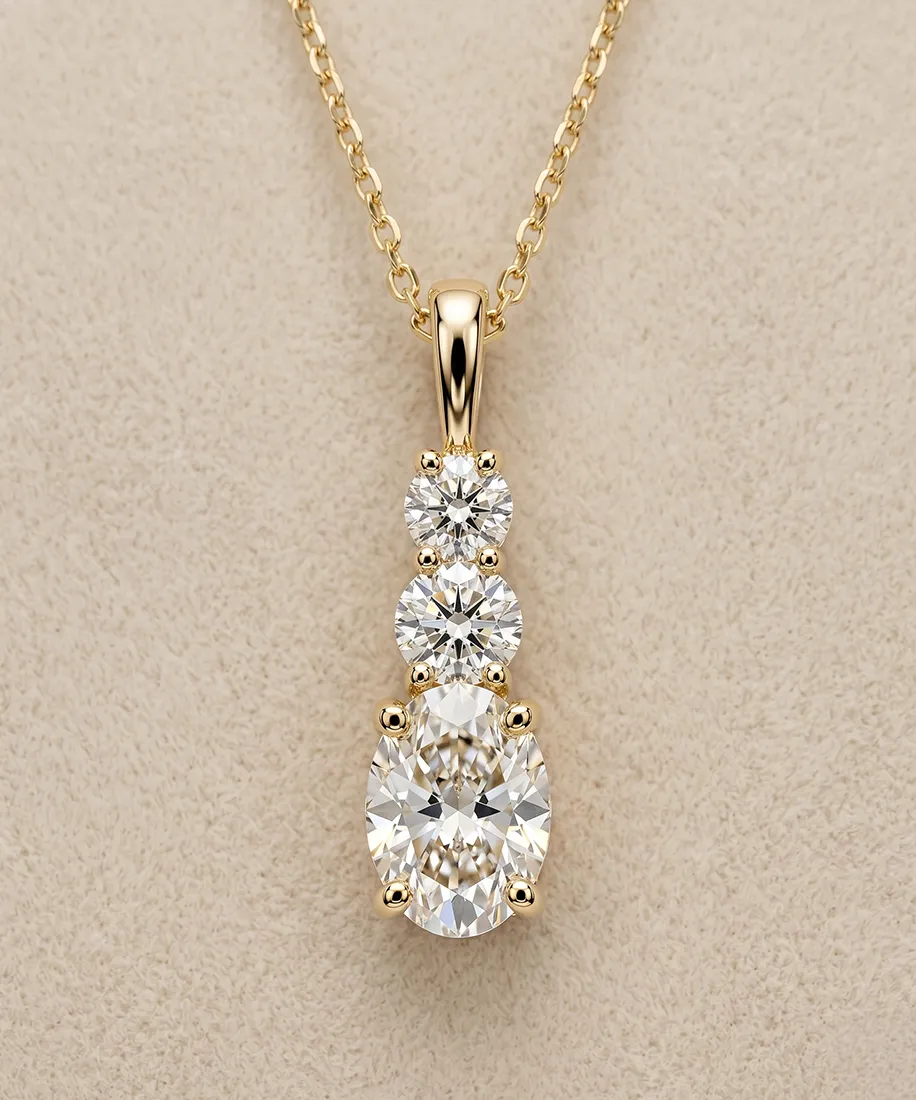 Gold necklace with three graduated diamonds on a beige background.