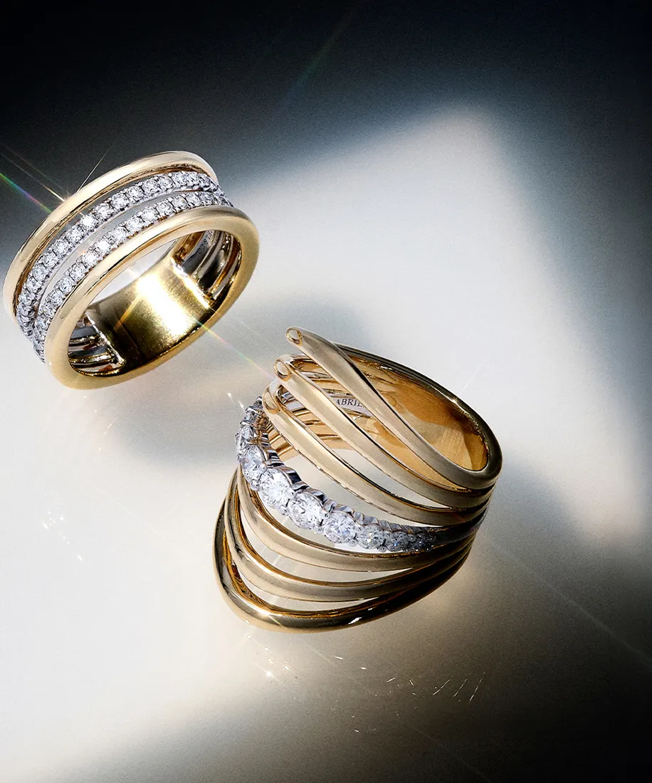 Two gold rings with diamond accents on a reflective surface.