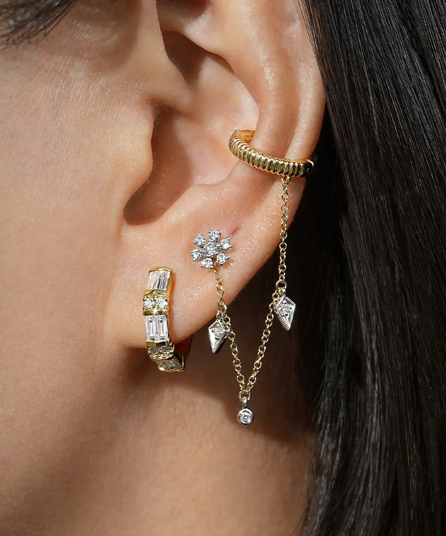 Close-up of an ear with multiple gold and diamond earrings, including a chain design.