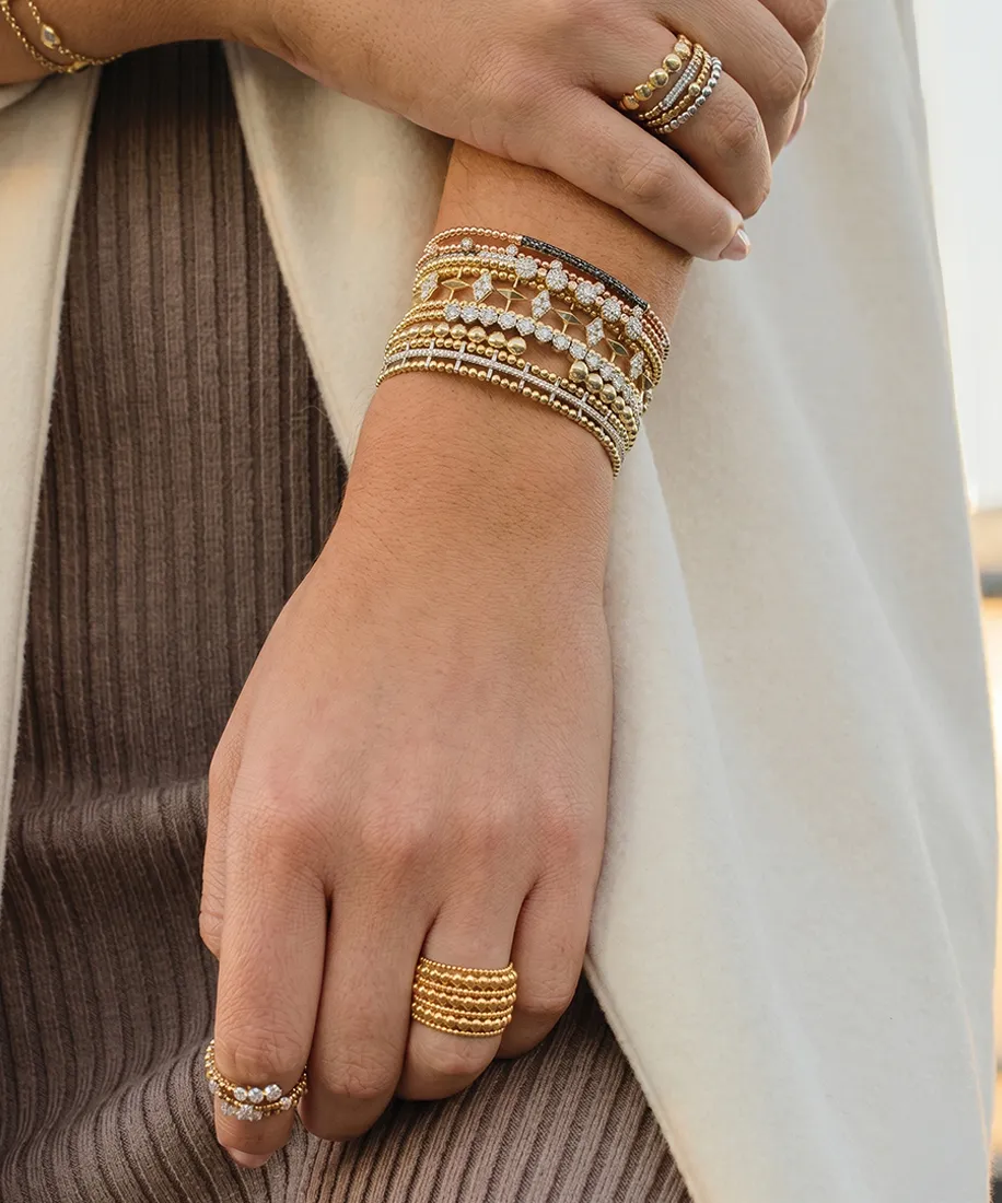 Stacked gold and diamond bracelets and rings on a woman's hands.