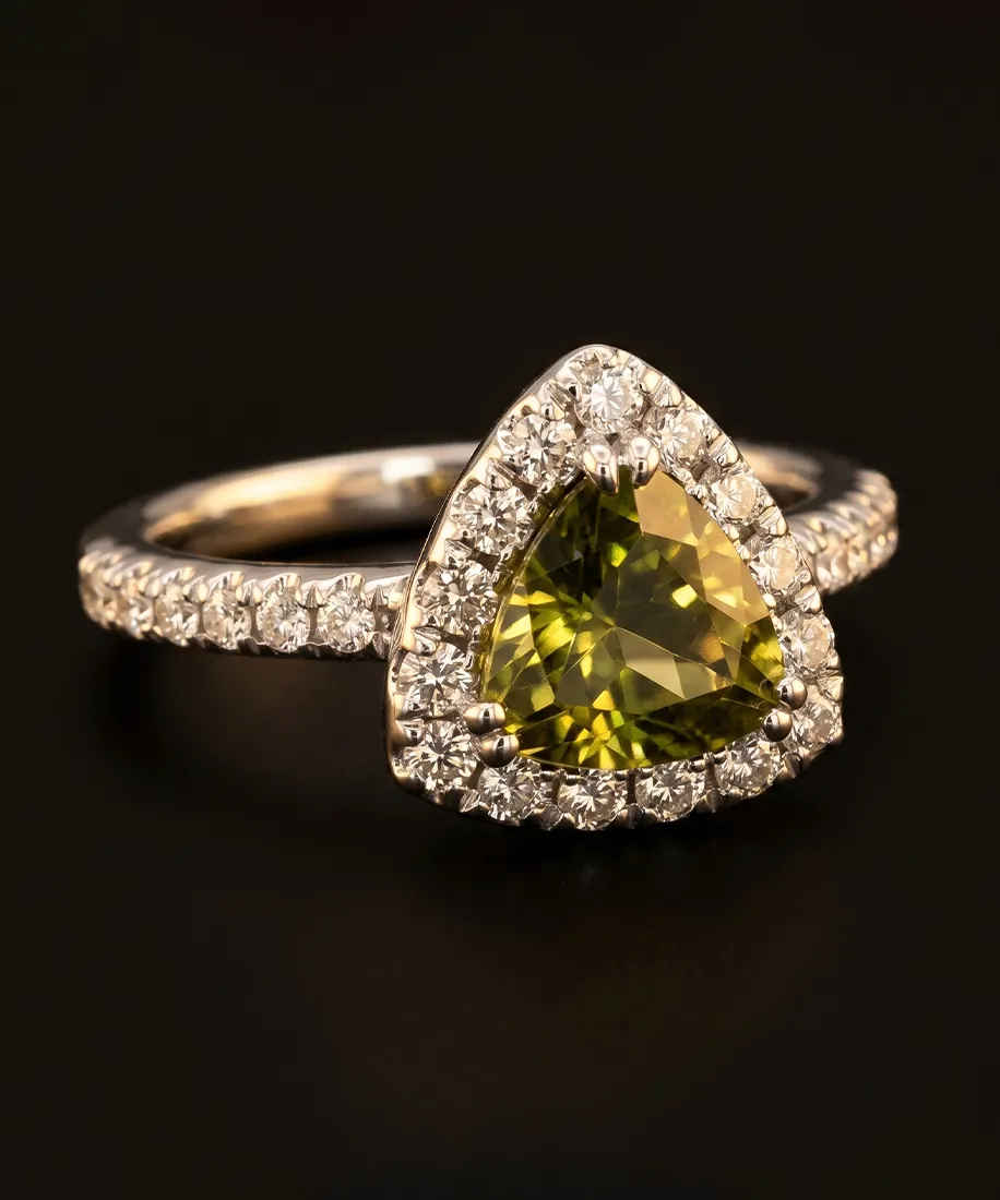 A triangle-cut green gemstone ring with diamond accents on a dark background.