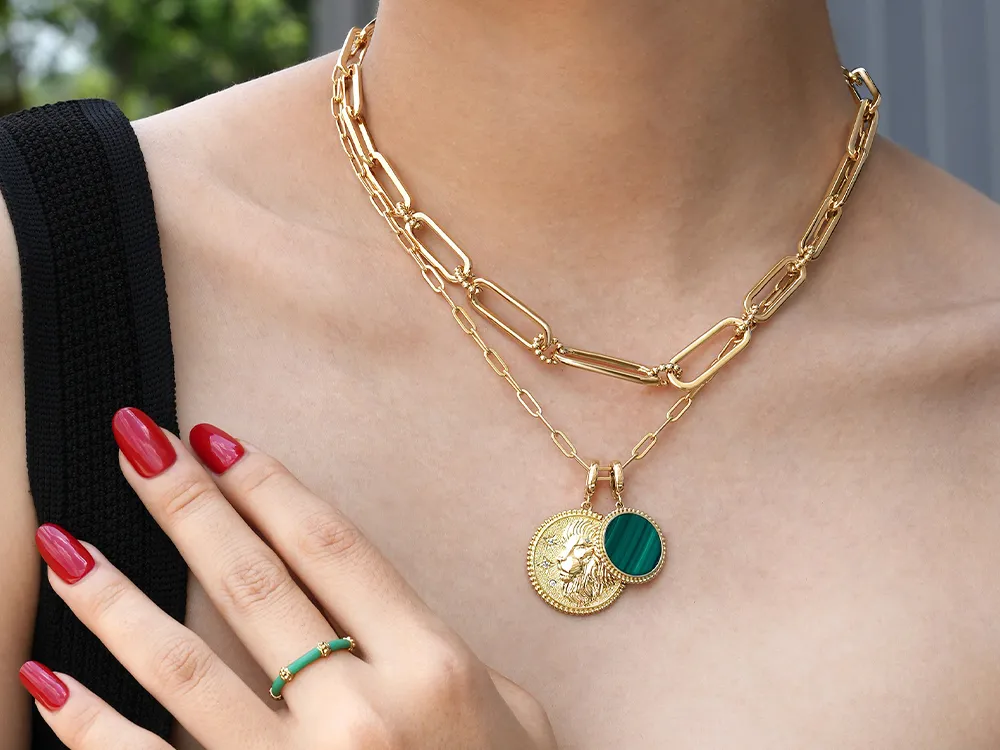 Gold chain necklace with coin and green pendant, red nails, and matching ring.