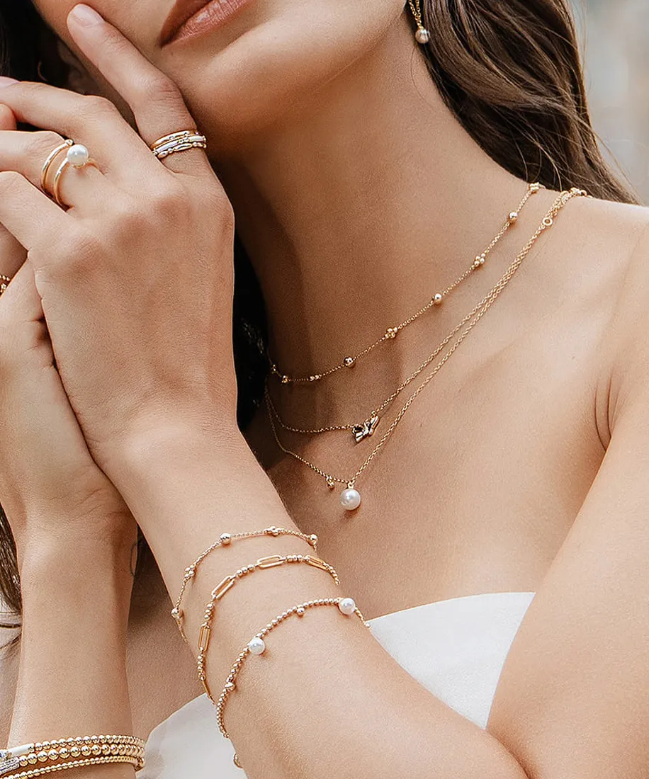 A woman wearing layered gold necklaces, bracelets, and rings with pearls.