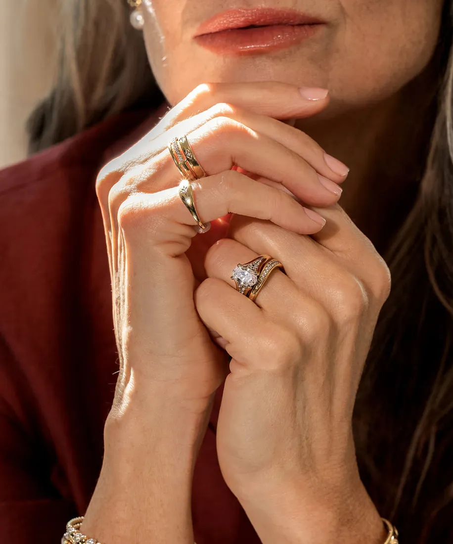 Close-up of a woman's hands with gold rings and a diamond ring, resting near her face.