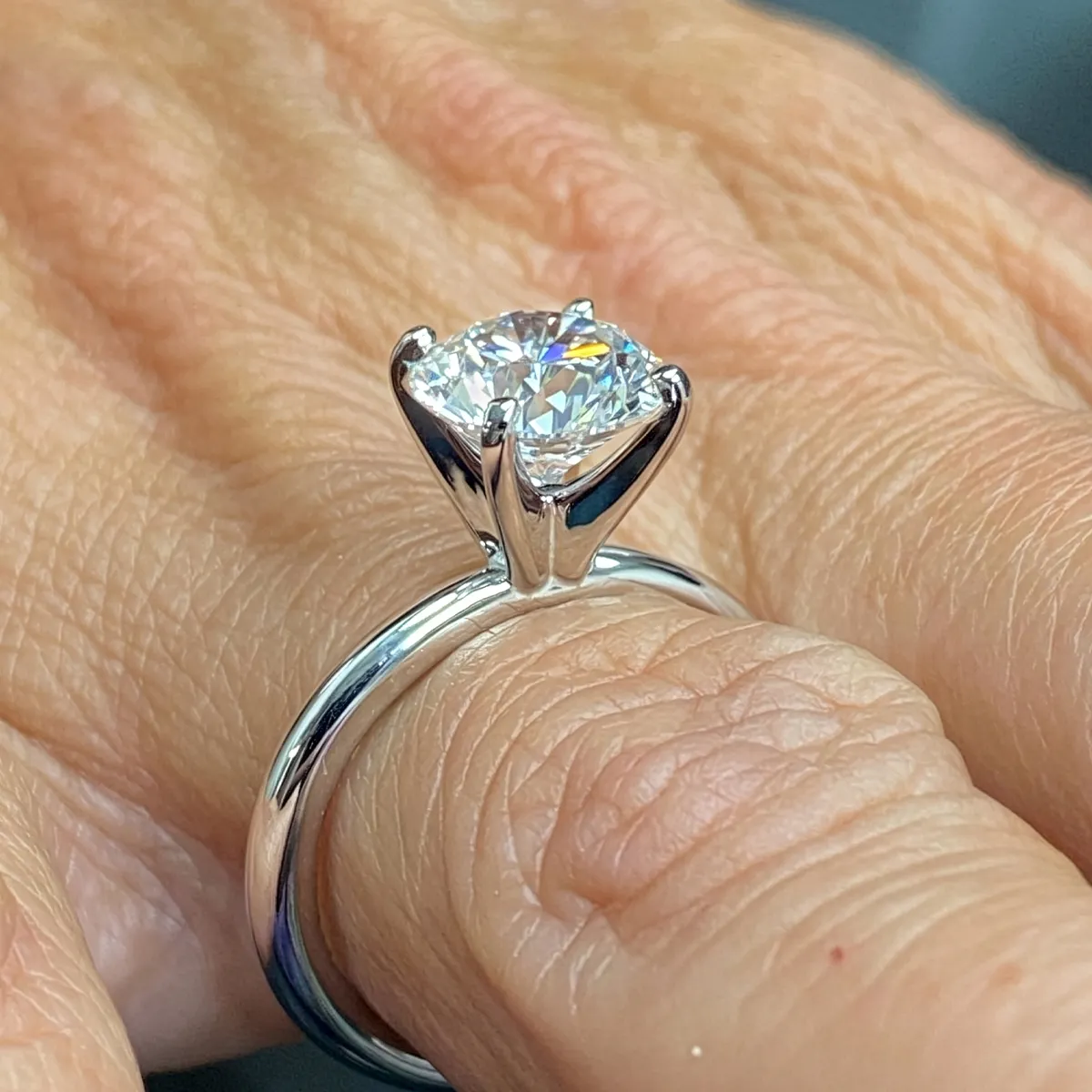 A close-up of a hand wearing a silver ring with a large diamond solitaire.