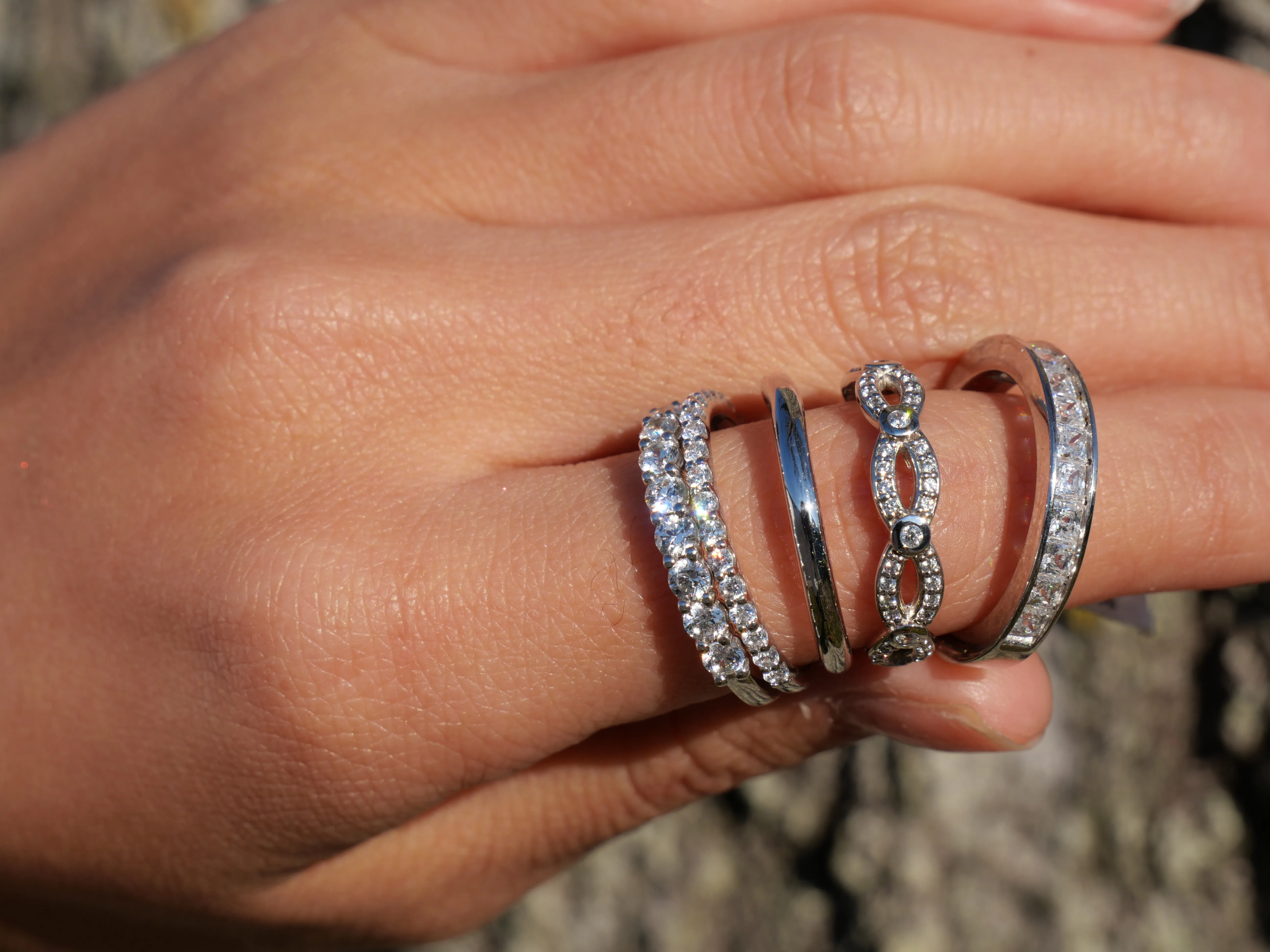 Four elegant rings with diamonds displayed on a hand. Visit Masterpiece Jewelers for fine jewelry and engagement rings.