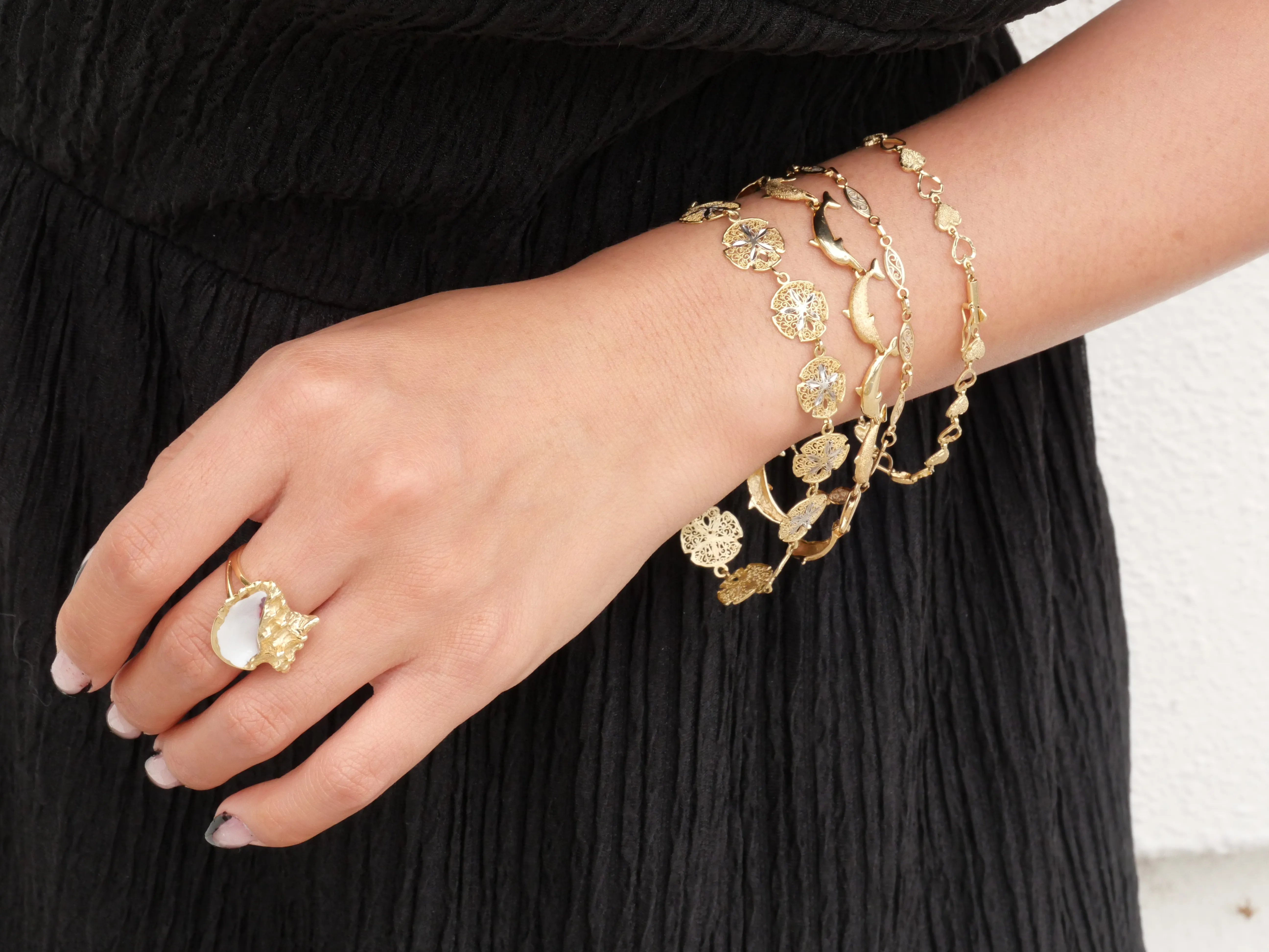 Elegant gold bracelets and a ring with gemstones on a hand. Explore more at Masterpiece Jewelers in Daytona Beach.