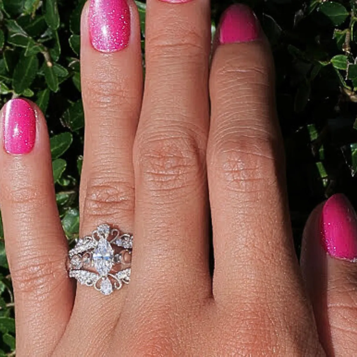 Elegant engagement ring with a floral design, featuring a central diamond and smaller stones, displayed on a hand.