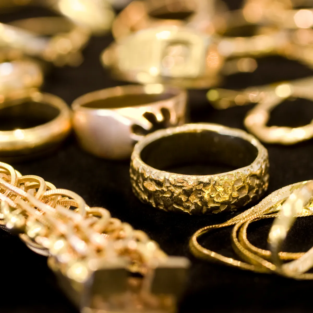 A collection of gold rings and jewelry pieces scattered. Click to explore gold buying at Masterpiece Jewelers.