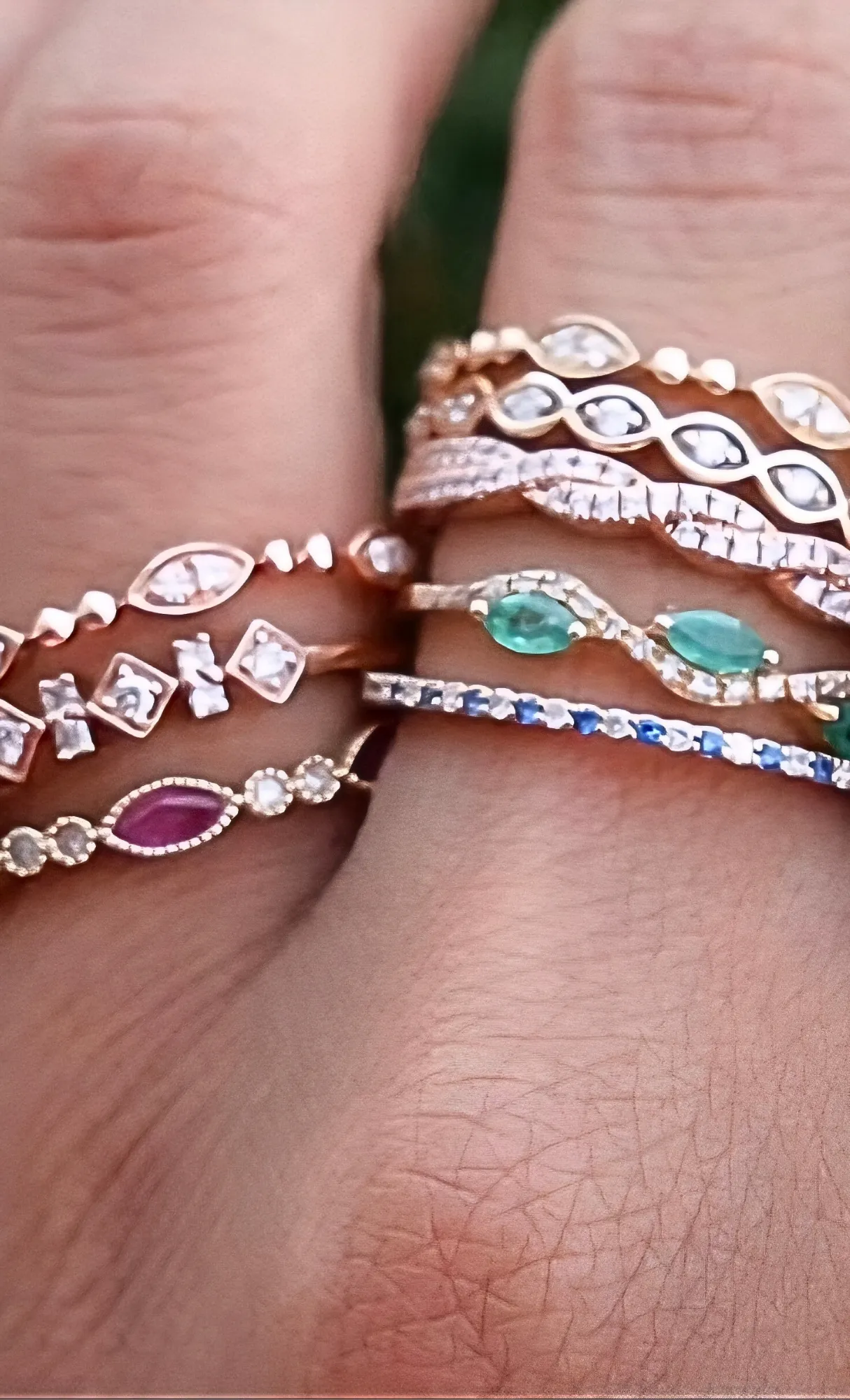 Elegant stack of diamond and gemstone rings on a hand. Shop now at Masterpiece Jewelers, Daytona Beach.