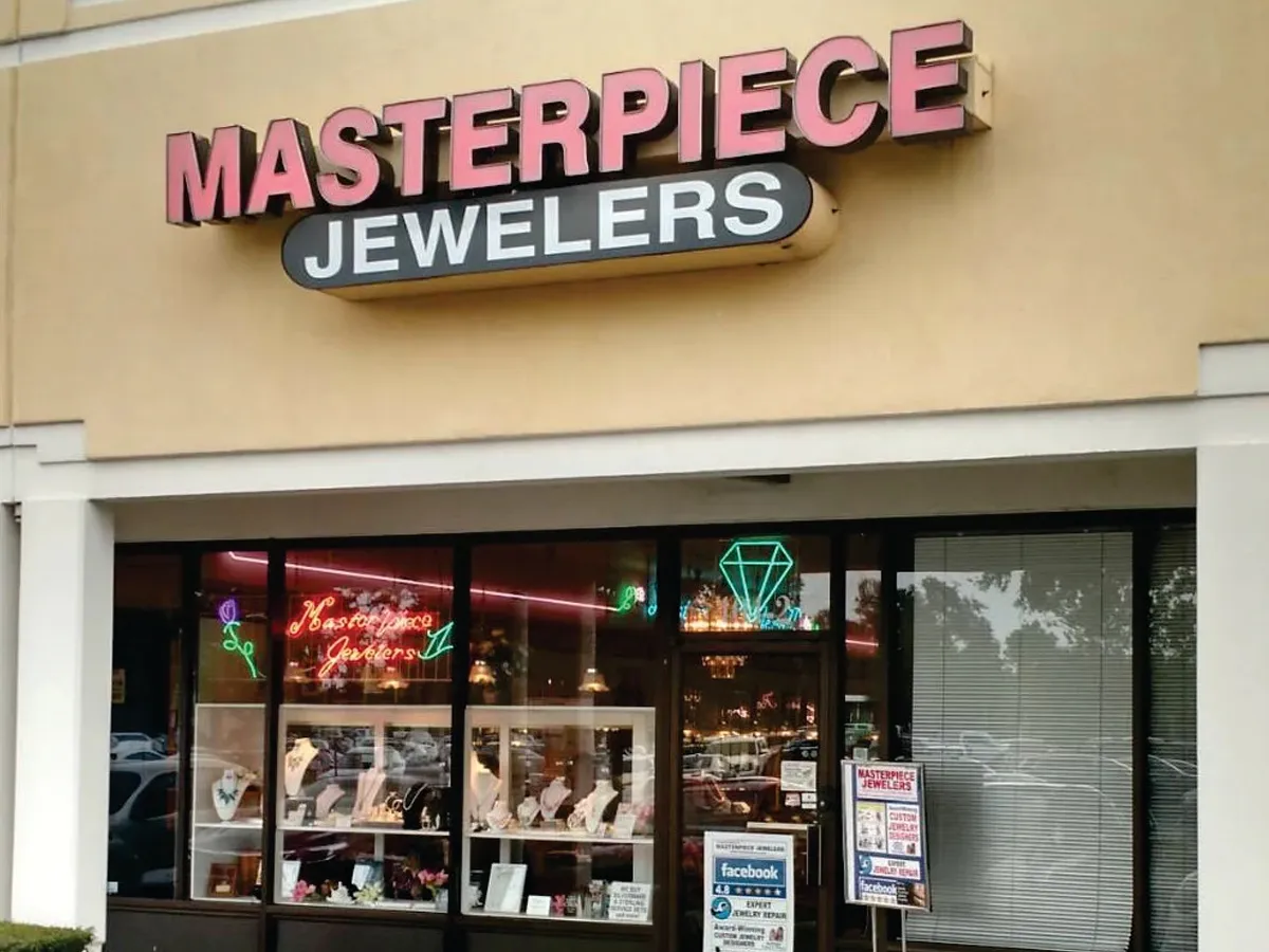 Masterpiece Jewelers storefront in Daytona Beach, showcasing fine jewelry and a neon sign. 
