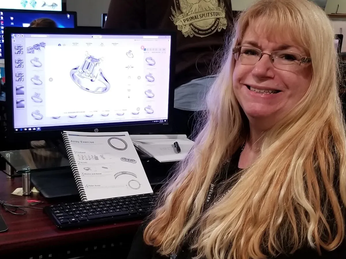 Tracy smiling at the camera while a computer with a 3D rendered engagement ring shows on the monitor.