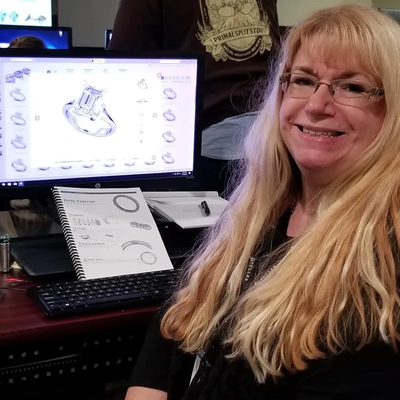 Tracy smiling at the camera while a computer with a 3D rendered engagement ring shows on the monitor.