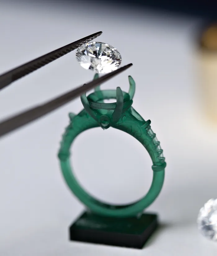 A diamond being placed into a green ring setting with tweezers, showcasing fine jewelry craftsmanship.