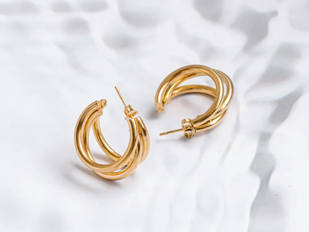 Gold hoop earrings with a twisted design, displayed on a textured surface. Perfect for adding elegance to any outfit.