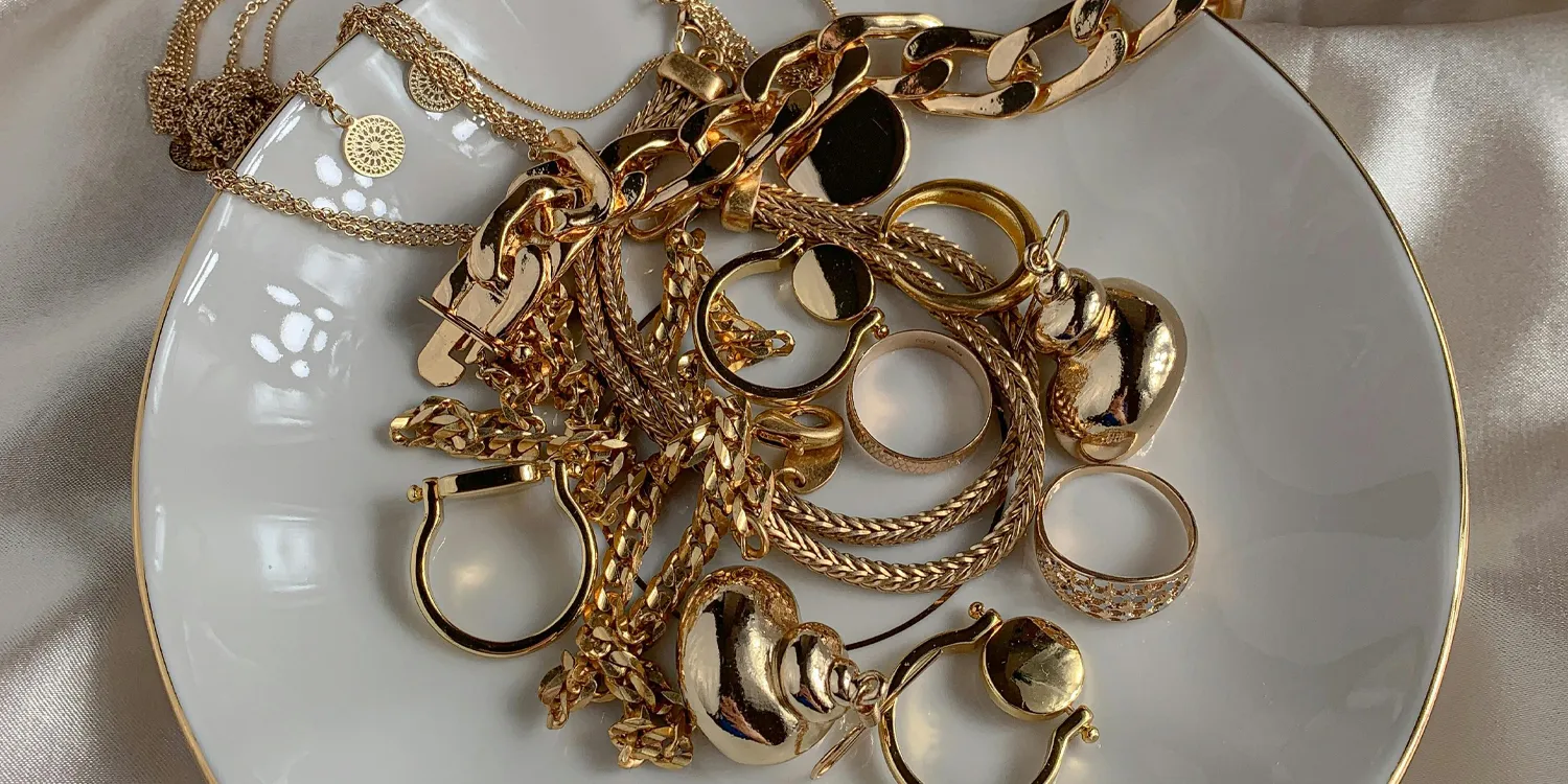 A collection of gold jewelry including rings, chains, and earrings displayed on a white plate.