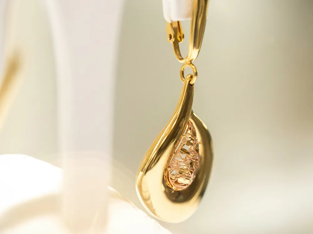 Gold teardrop earring with intricate design, showcasing a sparkling interior. Visit Masterpiece Jewelers for fine jewelry.
