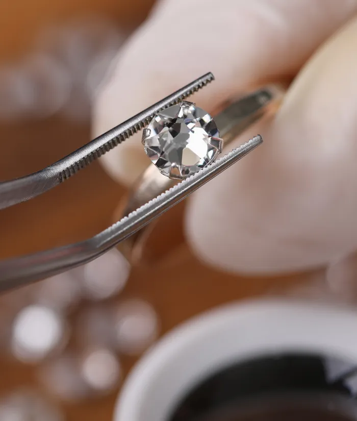 Jeweler using tweezers to hold a diamond ring for evaluation at Masterpiece Jewelers in Daytona Beach. Start a Project.