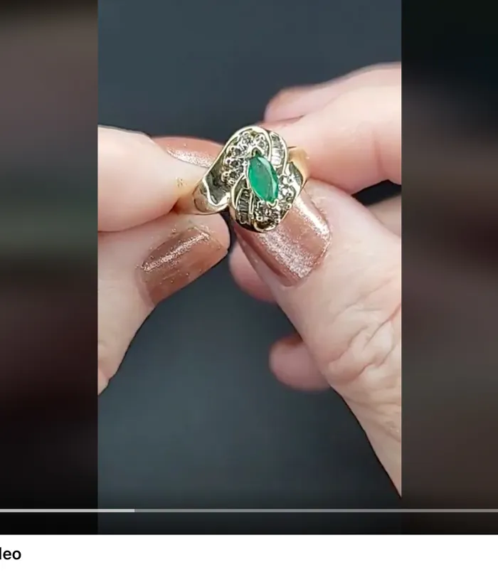 Hand holding a gold ring with a green stone, featured in a video by Masterpiece Jewelers.