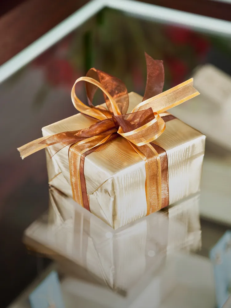 Gift-wrapped box with a brown ribbon on a reflective surface, showcasing Masterpiece Jewelers' gift wrapping service.