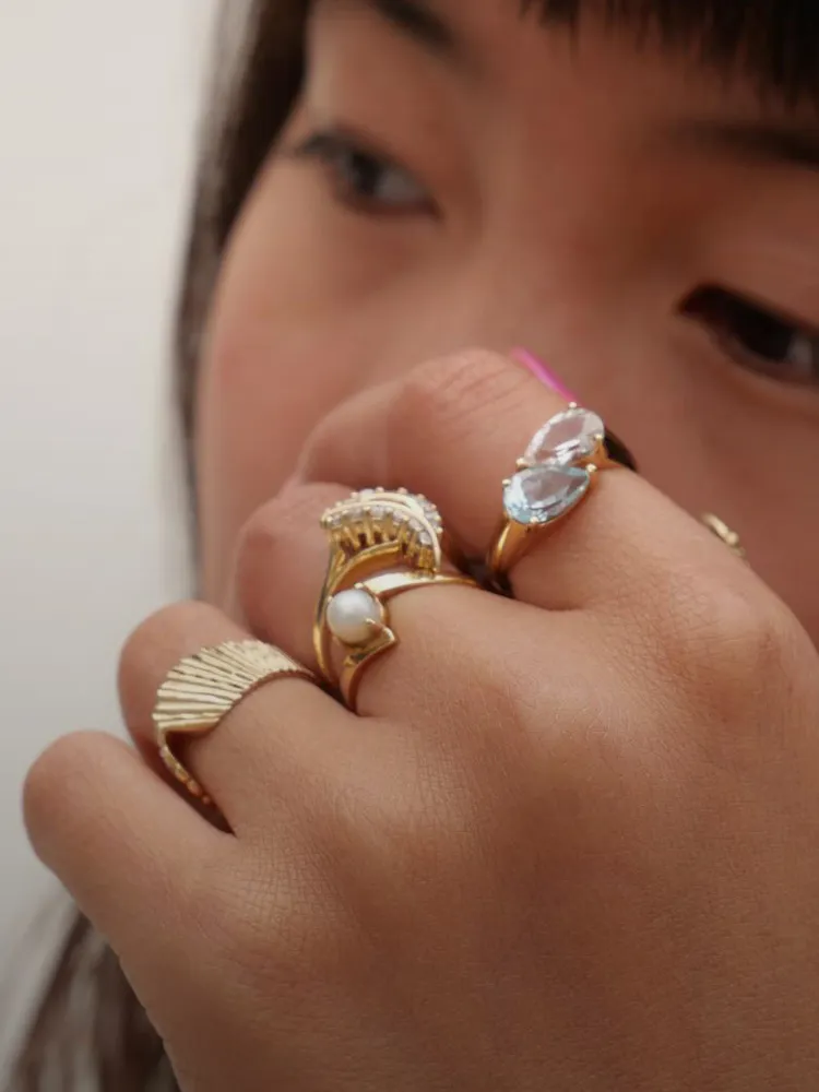 Close-up of a hand wearing multiple gold rings with gemstones. Shop fine jewelry at Masterpiece Jewelers in Daytona Beach.