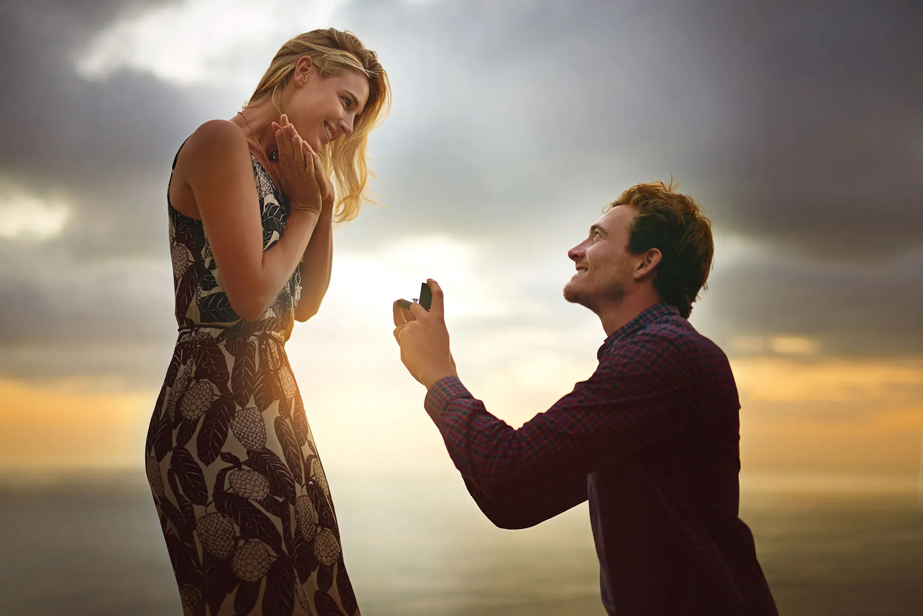 Couple engaged on a beach at sunset; man proposing with a ring. Click to explore bridal jewelry at Tipton's Fine Jewelry.