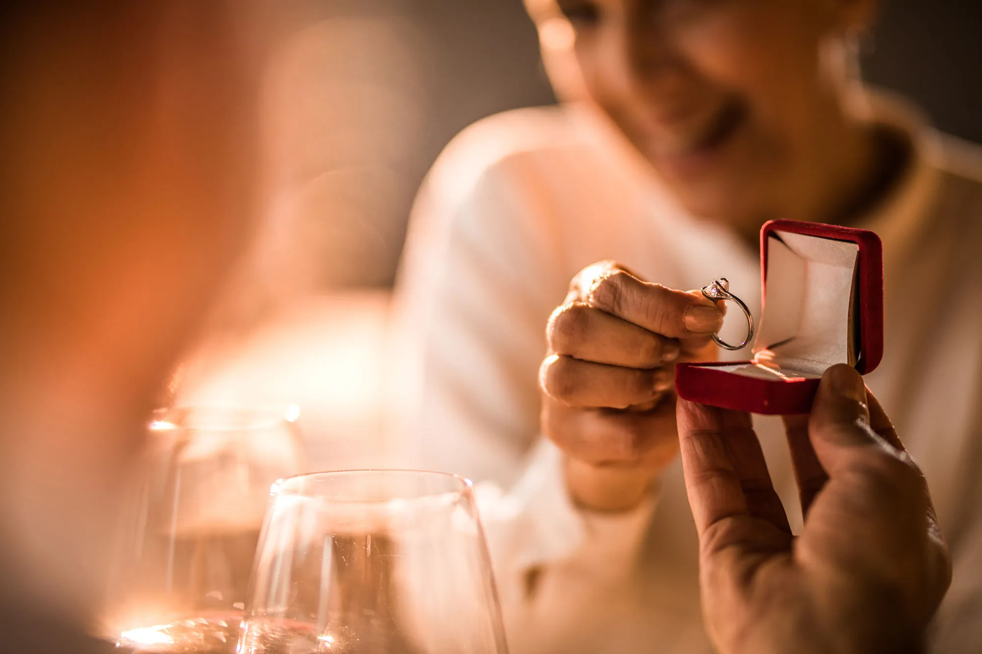 A woman joyfully presents an engagement ring in a red box during a romantic moment. Click to explore anniversary bands at Chippe