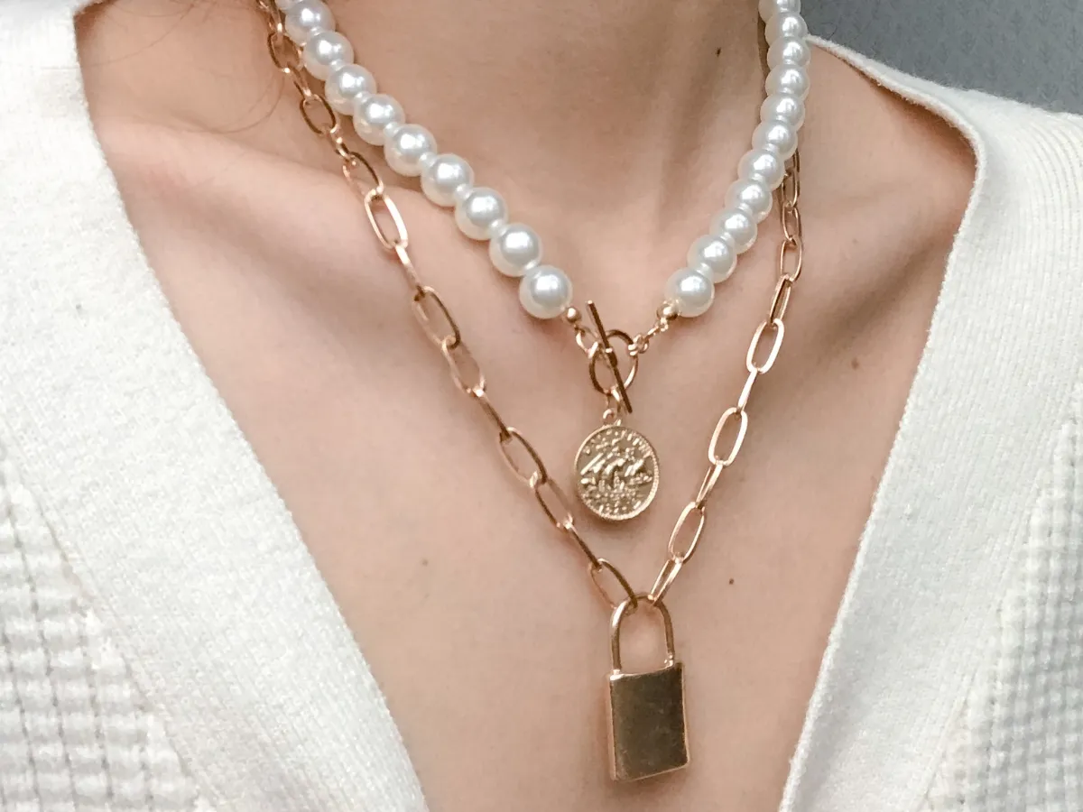 Layered pearl and gold chain necklace with lock pendant.