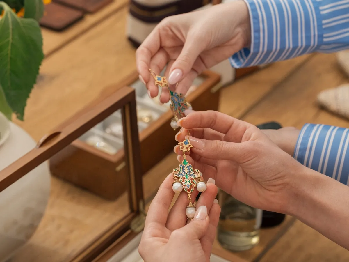Hands holding ornate drop earrings.