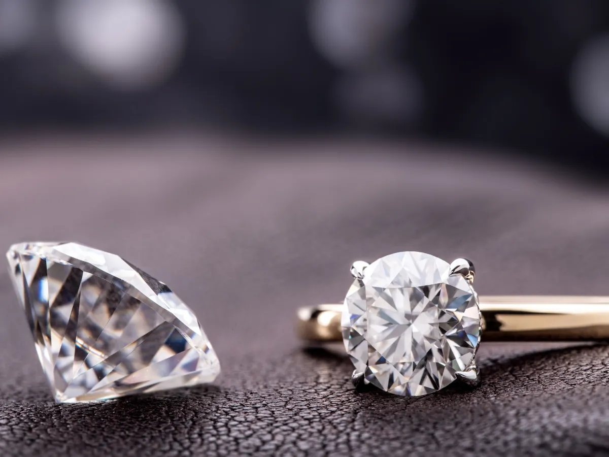 Loose diamond beside gold engagement ring.