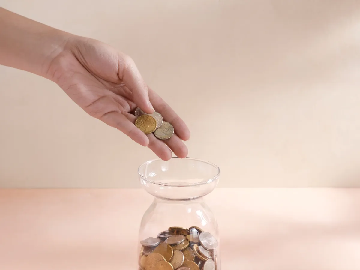 Hand dropping coins in jar.