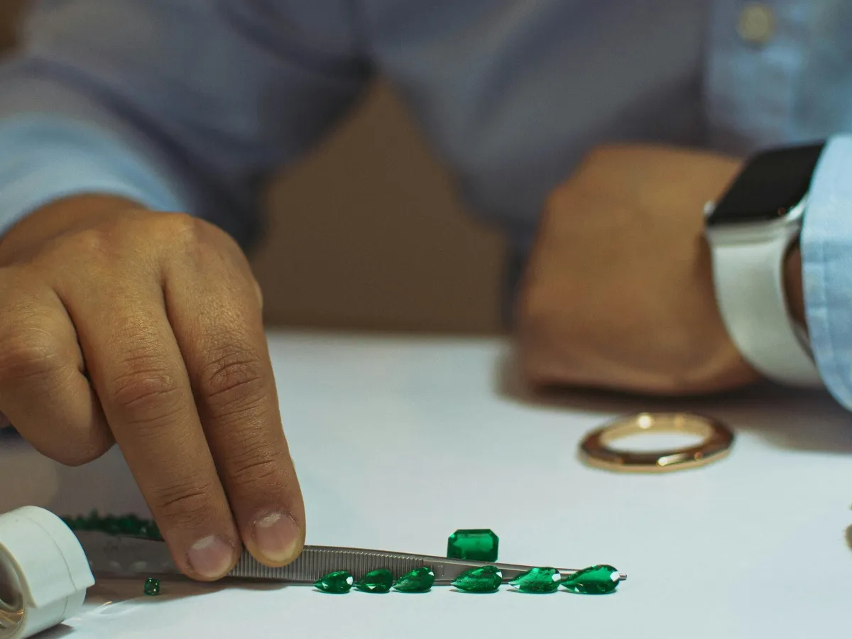 Hand inspecting green emerald gemstones.