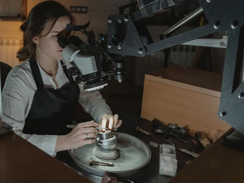 A jeweler working on a piece of jewelry and using a scope to magnify what she sees.