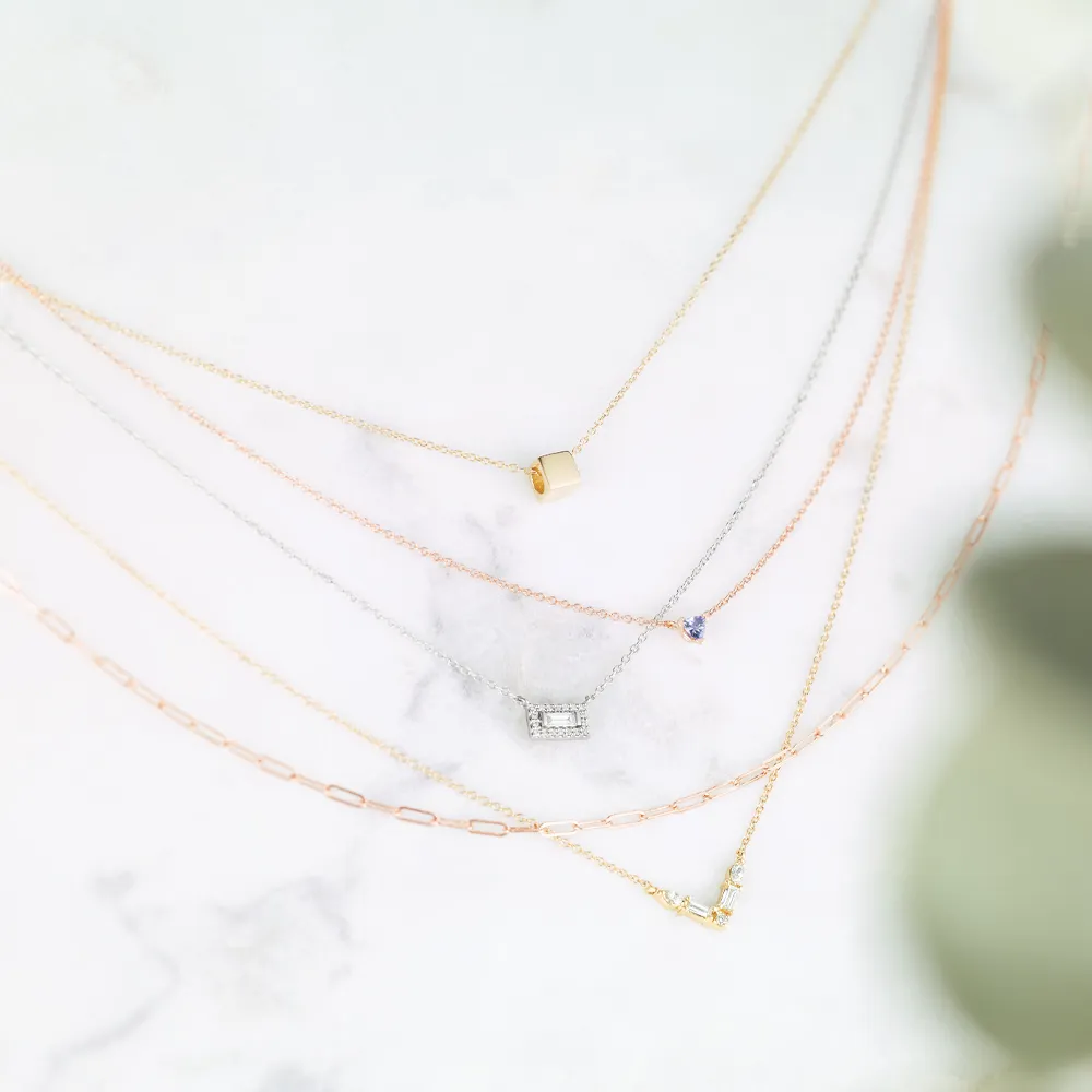 Multiple dainty necklaces laying on top of one another in various metal types such as gold, silver, and rose gold