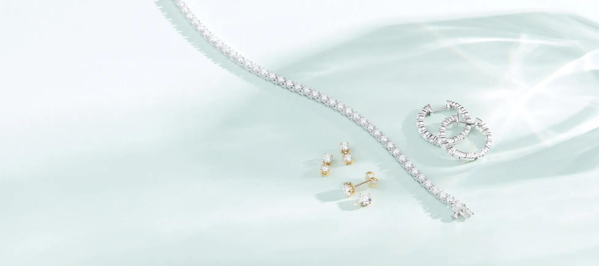 Diamond bracelet, stud earrings, and hoop earrings laying on teal surface