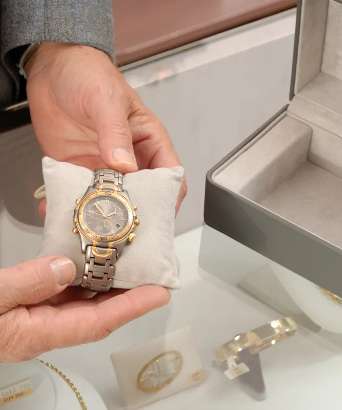 Man presenting a watch laying on a small plush pillow on top of a jewelry case seen in a jewelry store