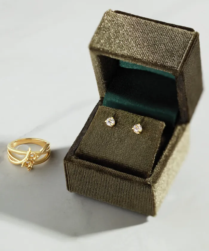 Diamond earrings in jewelry box with unfinished ring laying next to it on a marble surface