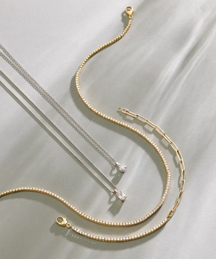 Gold and silver diamond necklaces laying on a beige background