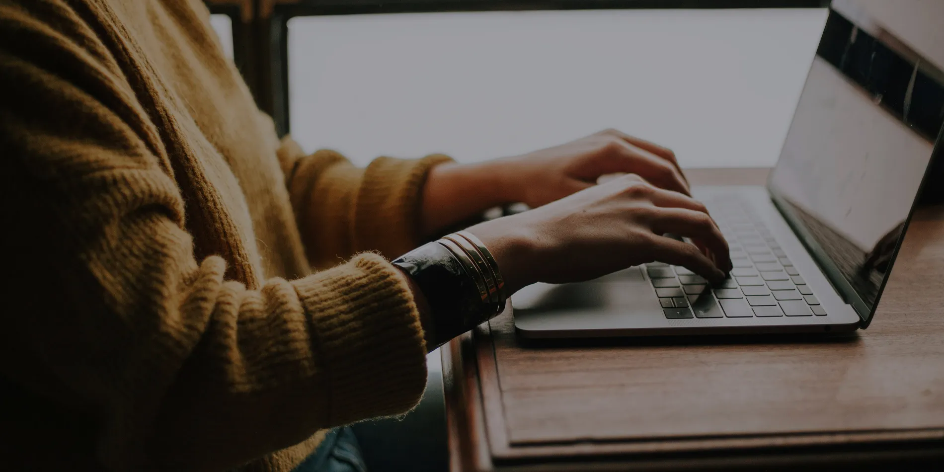 Woman wearing bracelets typing on laptop laying on a wooden desk
