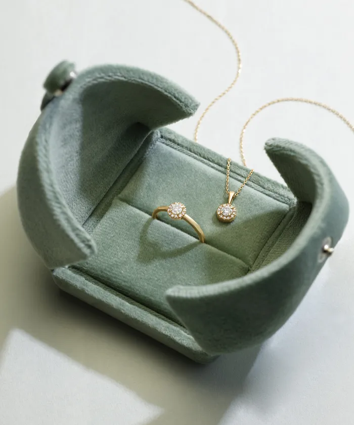 Gold diamond ring and necklace laying in and on a green ring box
