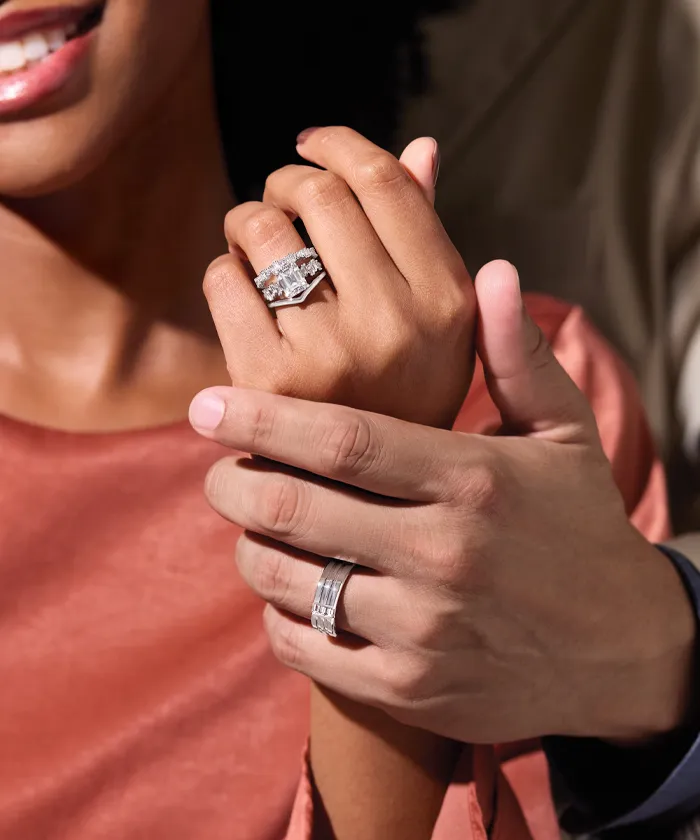 Man and woman holding each other while showing off their engagement ring and wedding bands