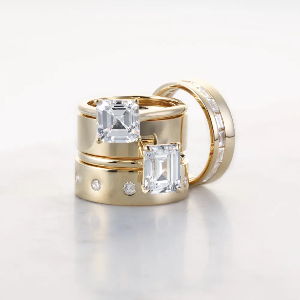 Emerald engagement rings with thick gold and diamond wedding bands on white surface