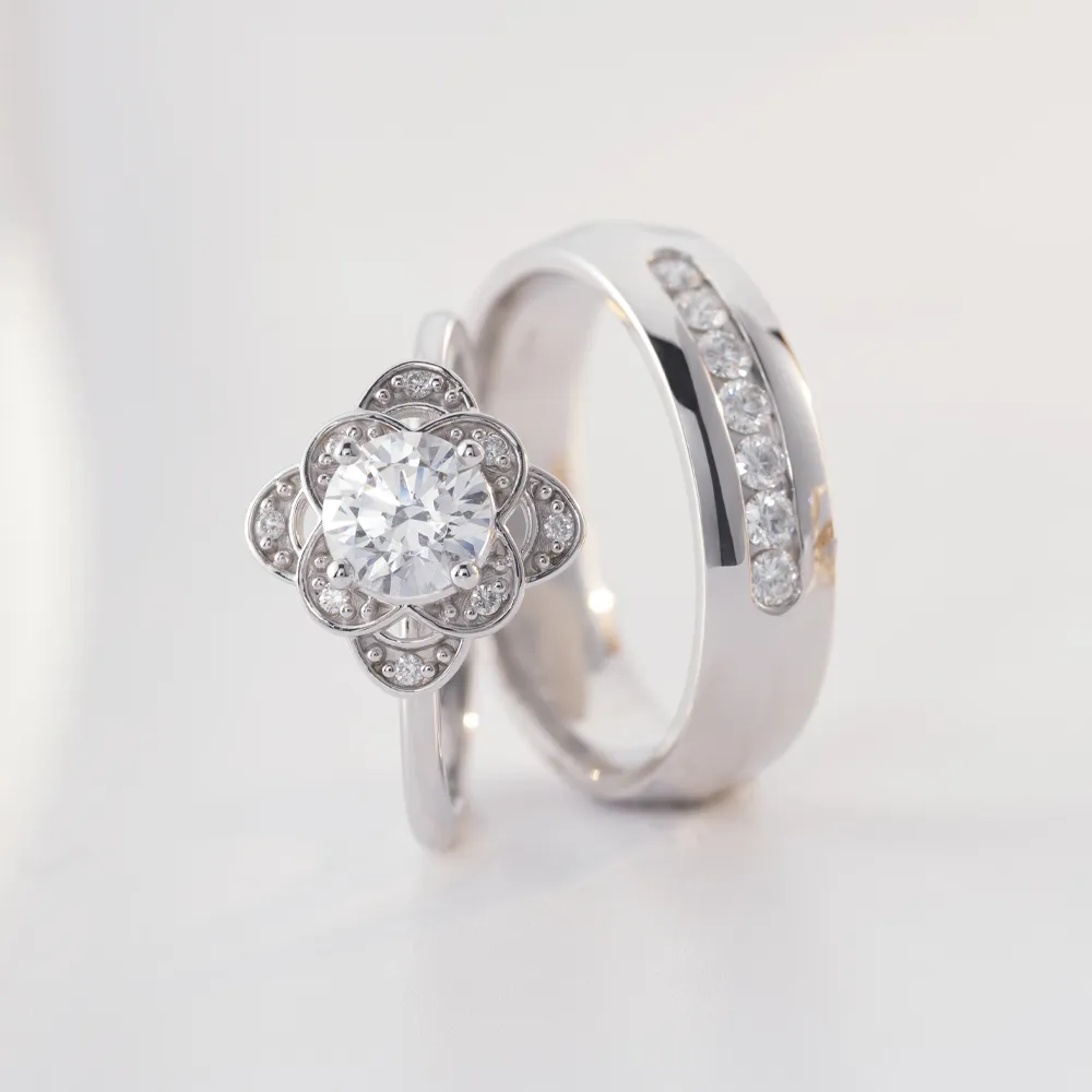 Round and flower diamond engagement ring with silver diamond wedding band on white surface